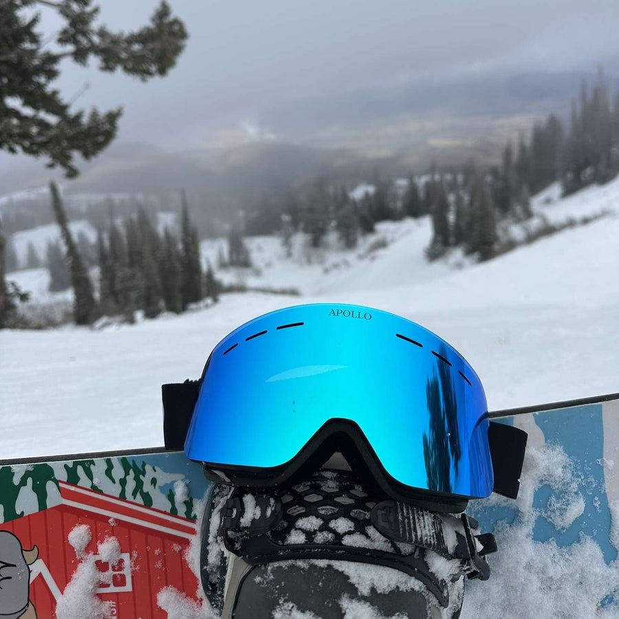 Blue ski goggles on a snowboard with a snowy mountain landscape in the background